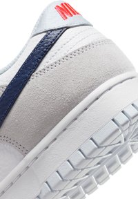 Sneaker med en texturerad grå mocka och vit läderöverdela, med en marinblå accentrand och röd logotyp. Tjock vit gummisula.