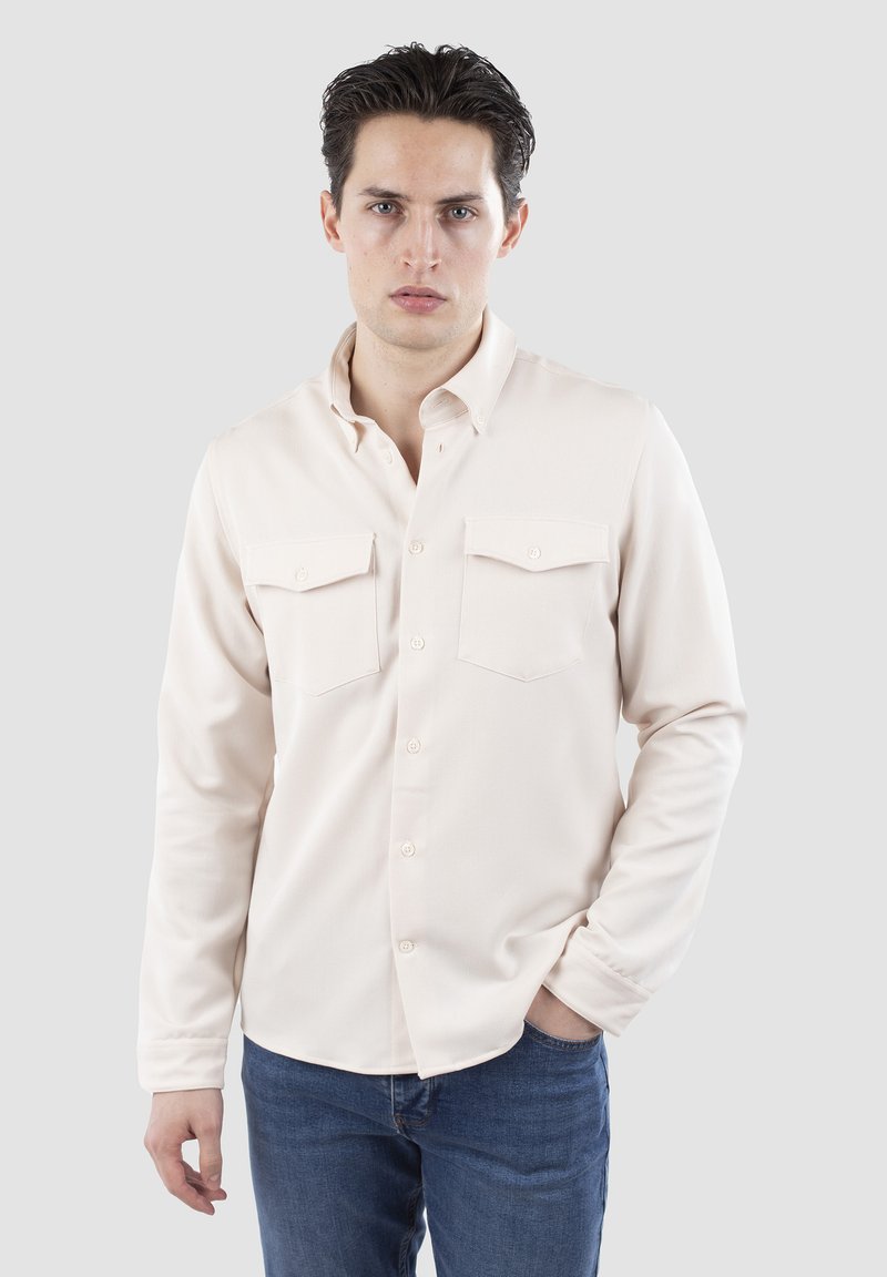 Creme langærmet skjorte med button-down krave, to brystlommer og knaplukning. Bæres med blå denim jeans. Glat tekstur.