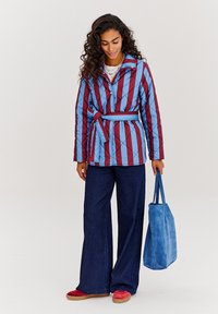 Prošívaná bunda s vertikálními červenými a modrými pruhy, páskovaná v pase. Spárována s tmavě modrými kalhotami širokého střihu a modrou semišovou kabelkou.