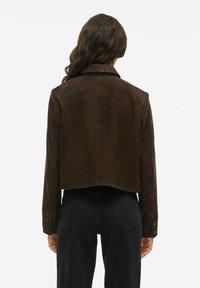 Brun ruskinds cropped jakke med klassisk krave, knapmanchetter og en glat overflade, vist fra ryggen med sorte jeans.