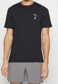 Svart kortärmad träningsskjorta i andningsbart material med rund halsringning, axelsömmar och en vit Puma-logotyp på bröstet.