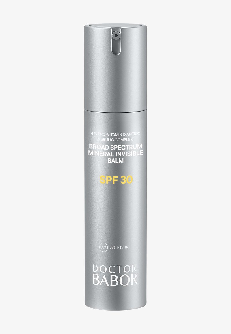 Conteneur cylindrique argenté avec un bouchon pompe, étiqueté "Baume Minéral Invisible à Large Spectre SPF 30", avec un texte blanc et jaune.