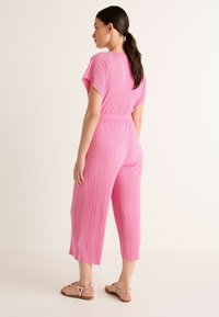 Rosa plisserad jumpsuit med korta ärmar, knytmidja, cropped ben och en slät yta, tillsammans med lätta sandaler.