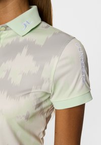 Koszulka polo w jasnym zielonym kolorze z teksturowanym wzorem w szaro-zielonej tonacji. Posiada kołnierzyk na guziki oraz haftowane logo na rękawie.