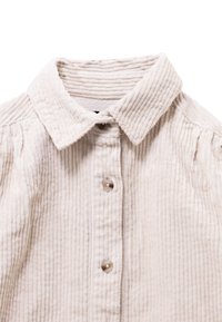 Beige corduroy overhemd met knopen en een spitse kraag, voorzien van een verticale ribbelstructuur en drie zichtbare knopen.