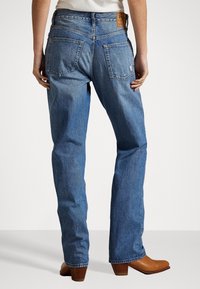 Jasnoniebieskie dżinsy o prostym kroju, z wyblakłą fakturą i widocznymi kieszeniami z tyłu. Posiadają brązową skórzaną łatę na pasie.