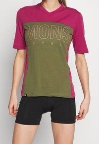 Tričko s krátkým rukávem a výstřihem do V v zelené a magentové barvě, s velkým potiskem "MONS ROYALE" v růžové, vyrobené z měkké látky s hladkou texturou.