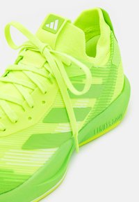 Neonowo zielone buty sportowe z teksturowanym wierzchem, cienkimi sznurowadłami i logo z trzema paskami. Posiadają grubą podeszwę oznaczoną "LIGHTSTRIKE."