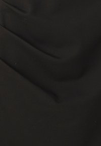 Tecido preto com uma textura suave, apresentando ligeiros drapeados e pregas, indicando um material leve e macio. Sem padrões ou destaques visíveis.