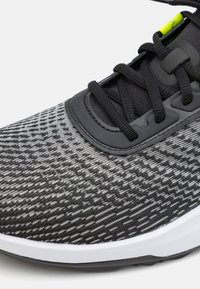 Buty sportowe z czarną i szarością dzianinową cholewką z teksturowanym wzorem, czarnymi sznurowadłami, gumową podeszwą i małym neonowym akcentem.