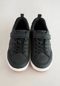 Czarne sneakersy o gładkiej fakturze, z perforowanym noskiem, płaskimi sznurowadłami i paskiem na rzep. Posiadają białą podeszwę i gumową podeszwę zewnętrzną.