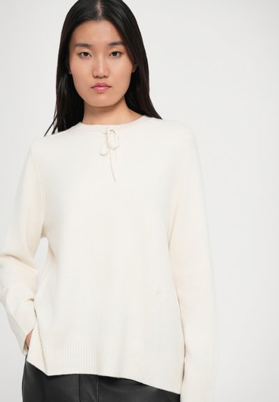 Cream-colored knit sweater with a round neckline, drawstring detail, and ribbed cuffs and hem, paired with black leather pants.
