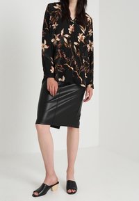 Black floral blouse with long sleeves paired with a black leather pencil skirt. Model wears black slide sandals with wooden heels.