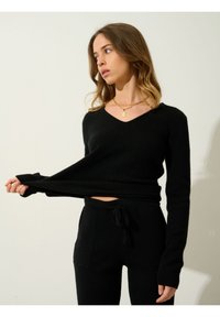 Suéter negro de punto con escote en V y mangas largas, combinado con pantalones negros a juego que tienen bolsillos frontales y cintura con cordón.