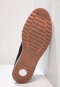 Dunkelblaue Wildlederschuhe mit einer strukturierten Gummisohle, die ein Blattmuster aufweist, und einem weißen kreisförmigen Logo an der Ferse.