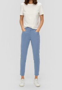 Pantalones de corte ajustado en un azul claro, con bolsillos laterales, un cierre de botón y una textura suave, combinados con una camiseta blanca de manga corta y zapatillas blancas.