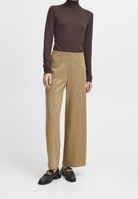 Col roulé marron à manches longues, pantalon à carreaux taille haute beige et marron, tissu texturé, associé à des mocassins noirs avec des détails dorés.