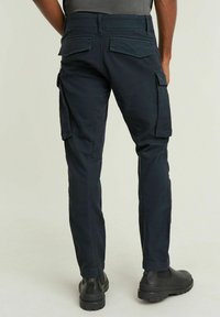 Ciemnoniebieskie spodnie cargo o slim fit, wykonane z wytrzymałego materiału. Posiadają duże boczne kieszenie oraz kieszenie z tyłu, a także gładką fakturę.