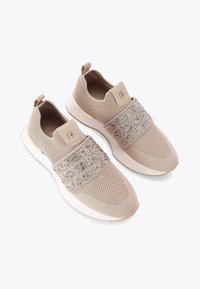 Sneakers in maglia beige con un design in rete testurizzata, dotati di dettagli metallici e una cintura scintillante attorno al mesopiede. Suola in gomma.