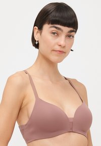 Formet BH i støvete rosa, laget av glatt stoff. Har justerbare stropper og en bred underkant for støtte, med sømløst design.