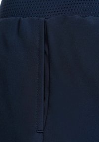 Acercamiento a una tela azul marino con una costura vertical y una abertura, mostrando la textura y los detalles de costura en el material.