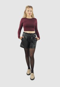 Bordeaux crop top met lange mouwen, gecombineerd met hoge zwarte nepleer shorts. Daarnaast doorschijnende zwarte panty met stippen en beige instappers.
