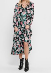 Kukkamekko, jossa on pitkät hihat, musta tausta, vaaleanpunaisia ja teal-värejä sisältäviä kukkia, V-pääntie ja taskut. Yhdistetty mustien nilkkasaappaiden kanssa.