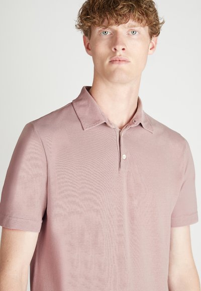 Korte mouwen polo shirt van zacht, lichtroze stof. Voorzien van een klassieke kraag en een knopsluiting met twee knopen met subtiele structuur.