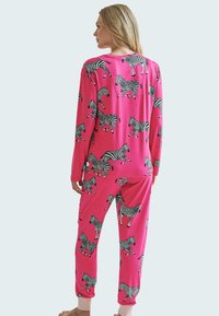 Růžový pyžamový set z měkké tkaniny, zdobený zebřími vzory v černé a bílé barvě. Dlouhé rukávy a kalhoty s elastickými manžetami.