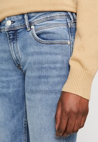 Ljusblå jeans i denim med klassisk femficksdesign, subtila blekningar och kontrasterande sömmar. Ribbad beige tröjärm synlig.