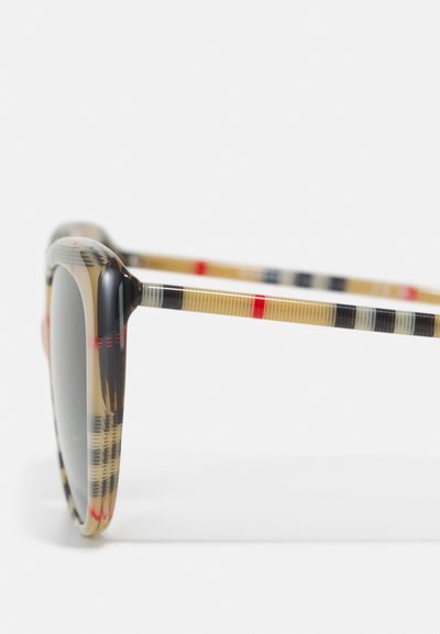 Lunettes de soleil avec un motif à carreaux noir et beige, monture en plastique et verres gris. Les branches présentent des rayures de couleurs alternées.