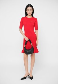Röd ribbad klänning med korta ärmar och utsvängd fåll, kombinerad med en svart läderhandväska med böjt handtag och gulddetaljer.