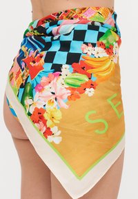 Bufanda de seda con vibrantes patrones florales, diseño de tablero de ajedrez y un fondo dorado con letras "SE" en verde a lo largo del dobladillo.