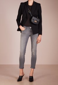 Blazer negro ajustado sobre una blusa negra, combinado con jeans grises con los puños doblados y mules negros. Un pequeño bolso de hombro negro completa el look.
