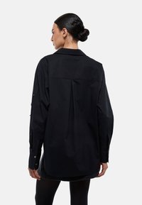 Chemise noire surdimensionnée, en tissu coton, dotée de manches longues avec poignets à boutons, d'un pli au dos pour plus de mouvement, et d'un col pointu.
