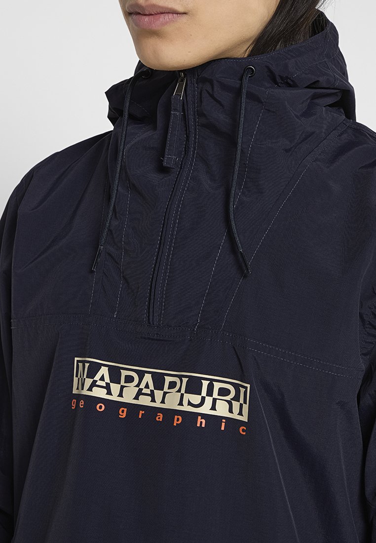 Persona vestida con una chaqueta con capucha de color azul marino y media cremallera, con el logo "NAPAPIJRI geographic" en el pecho y cordones en la capucha.