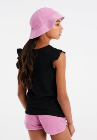 Sort struktureret top med flæseærmer parret med lyserøde terrycloth shorts. En lyserød bucket hat fuldender looket.