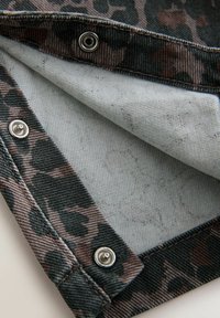 Leoprint-Denim mit grauem Innenfutter, ausgestattet mit silbernen Druckknöpfen und kontrastierenden Texturen zwischen Außen- und Innenstoff.