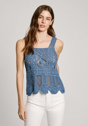Crochet blue tank top featuring a square neckline, open patterns, scalloped hem, and wide straps paired with white pants.