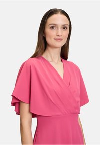Rosa Kleid mit kurzen, flatternden Ärmeln und einem V-Ausschnitt. Der Stoff ist glatt und hat Drapierungsdetails im Oberteil.