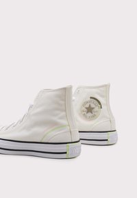 Witte canvas hoge sneakers met pastelaccenten, een zwart-wit gestreepte zool en een ronde Converse-logo op de hak.
