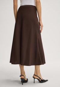 Jupe midi marron en forme A avec une texture lisse et une ceinture élastique, associée à des chaussures à talons noires avec des brides de cheville.