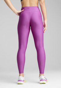 Tætsiddende lilla leggings med høj talje, lavet af glat, strækbart materiale. Har flade sømme og et logo nær taljebåndet.