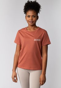 Rustkleurig t-shirt van zacht stof, met korte mouwen en een ronde hals, met witte tekst die zegt "Das Leben ist kein Ponyhof."