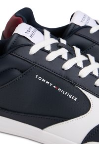 Baskets Tommy Hilfiger bleu marine et blanches avec lacets blancs, logo sur le côté et doublure rouge à l'intérieur de la zone du talon.