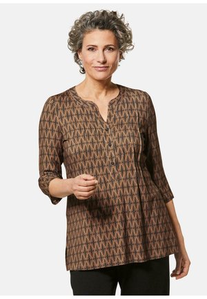 Braune Tunika mit geometrischem Muster, Rundhalsausschnitt, dreiviertel Ärmeln, Knopfverschluss und gefälteltem Design. Weiche Stofftextur.