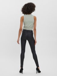 Černé vysoké skinny džíny s kapsami a hladkým povrchem, doplněné světle zeleným žebrovaným topem. Modelka má na sobě černé podpatky.
