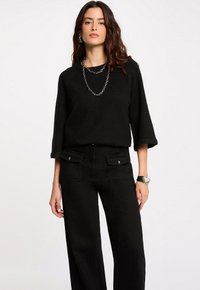 Maglione nero lavorato a maglia con maniche a tre quarti abbinato a pantaloni neri a vita alta con tasche frontali e dettagli metallici.