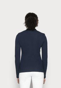 Marinblå långärmad topp med en figurnära design, rund halsringning och sidoklipp vid fållen. Tillverkad av en mjuk, elastisk bomullsblandning.