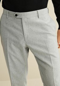 Hellgraue, maßgeschneiderte Hosen aus strukturiertem Stoff mit flacher Vorderseite,seitlichen Taschen und einem Knopfverschluss am Bund.